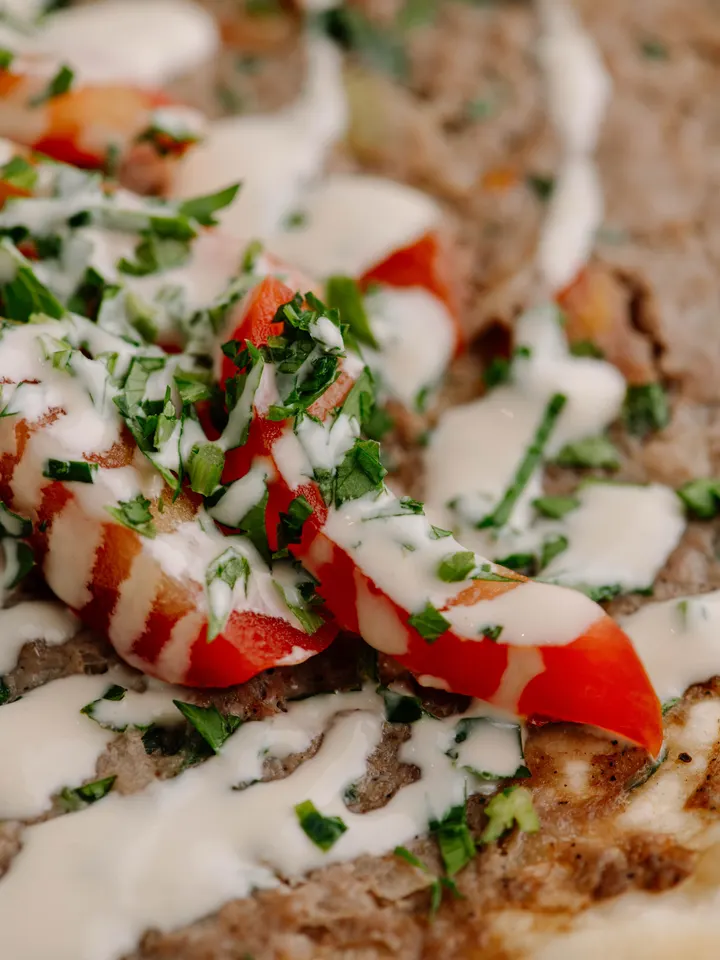 Primo piano di una manoucé al kebab con pomodoro, prezzemolo e salsa tahina